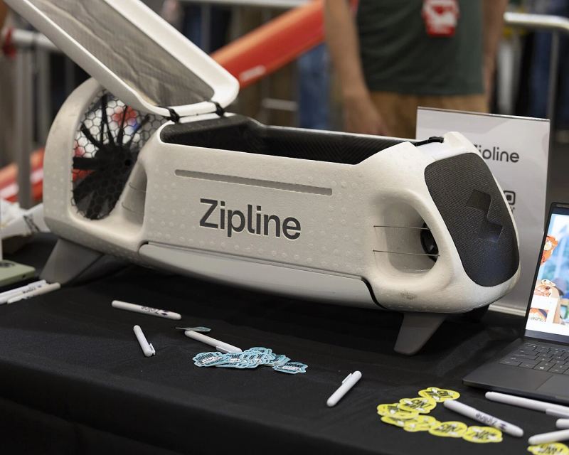 Zipline autonomous delivery aircraft on public exhibition showcasing wingspan, sensor arrays, and aerodynamic cargo housing.