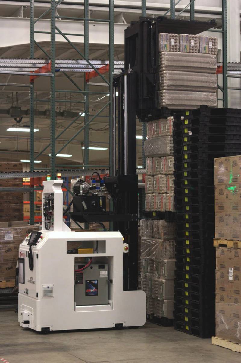 Automated guided vehicle forklift system operating autonomously in an industrial logistics facility.